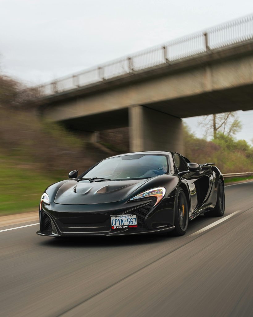 High-performance black McLaren sports car racing under a bridge on an open highway.